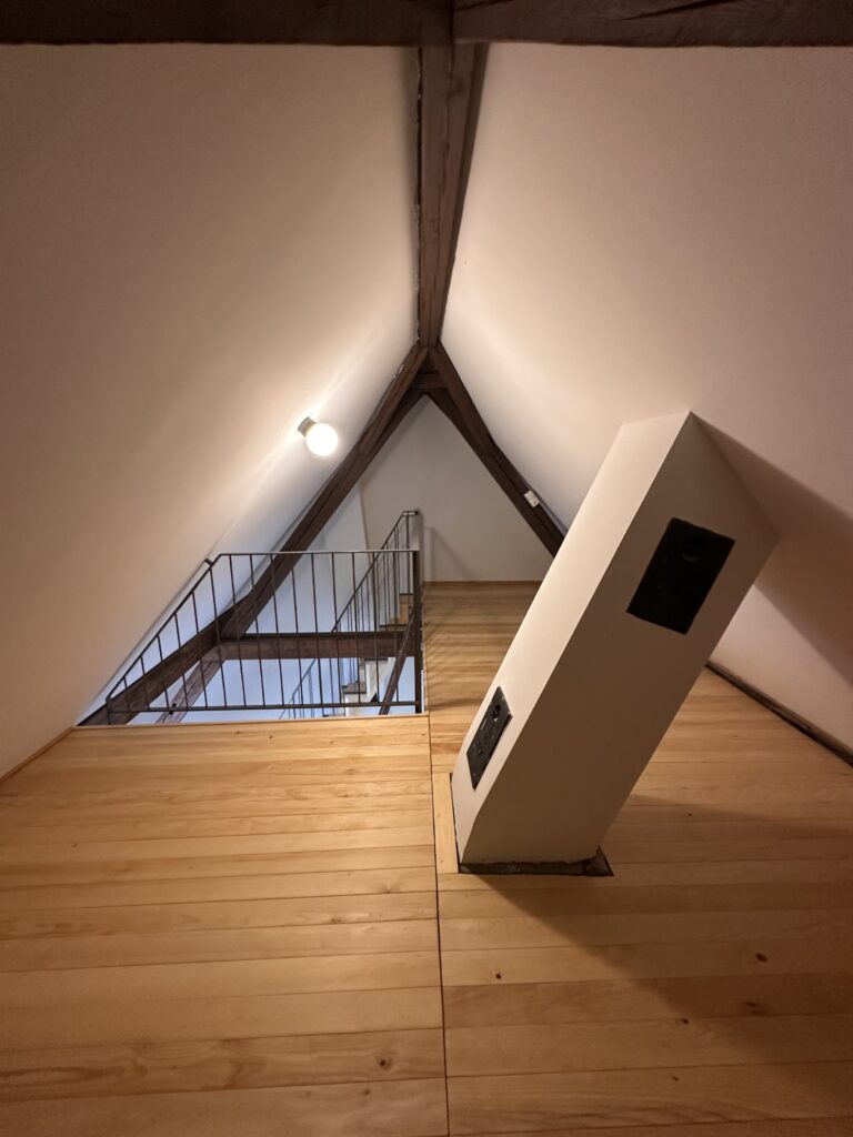 Ausgebauter Dachboden mit neuem, hellem Holzboden, weissen Wänden und sichtbaren, aufgefrischten Holzbalken.