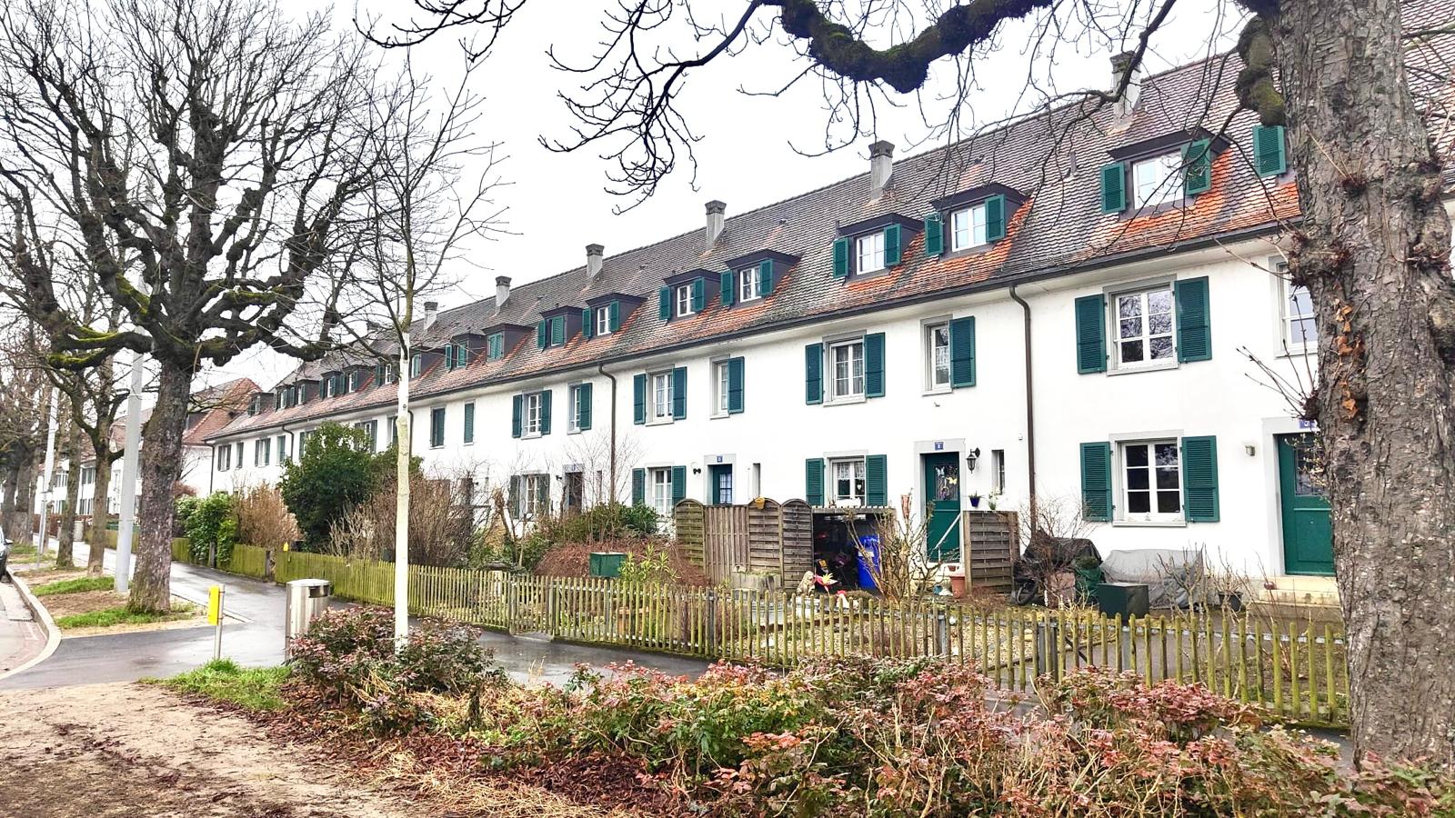 Aussenansicht der historischen Reihenhäuser an der Egliseestrasse in Basel mit weisser Fassade und grünen Fensterläden.
