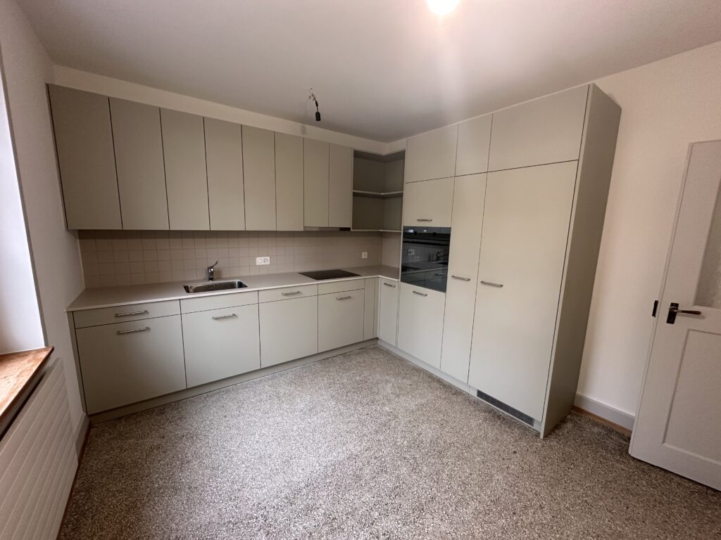 Moderne Küche mit grifflosen, beigen Fronten und fachgerecht aufgearbeitetem, originalem Terrazzo-Boden nach dem Umbau in Basel.
