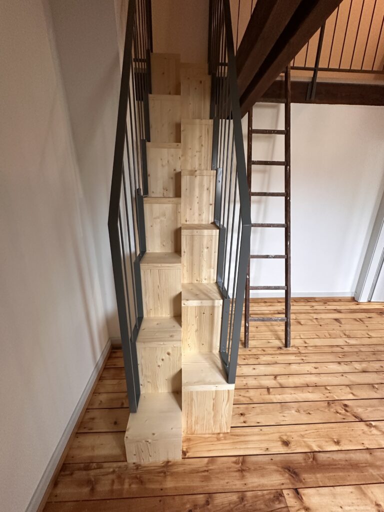 Massgefertigte, platzsparende Holztreppe mit anthrazitfarbenem Metallgeländer im neu gestalteten Dachgeschoss.